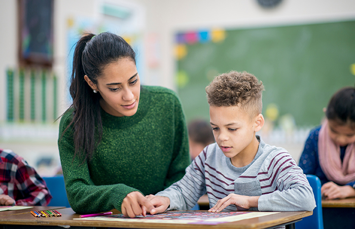 Primary teacher helping young boy in class