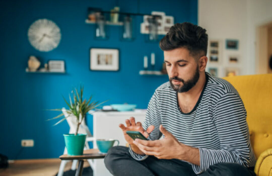 Young man seated on a yellow sofa using his smartphone