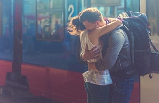 Coming to Ireland, man with a backpack hugging a woman beside a blue and red train