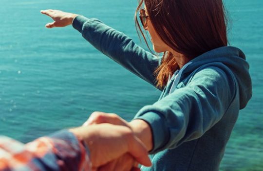 Young woman pointing the sun with her right hand on a side of the sea