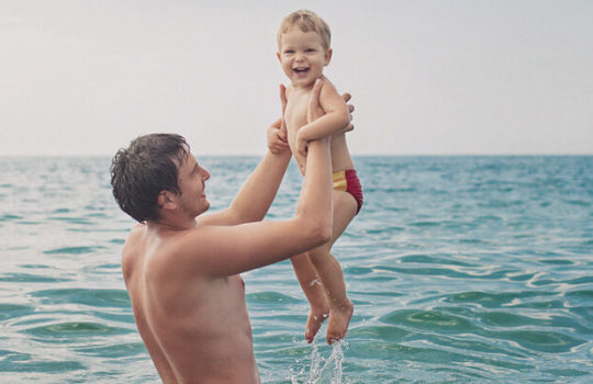 Life moments, planning your retirement, man holding toddler in both hands in the sea