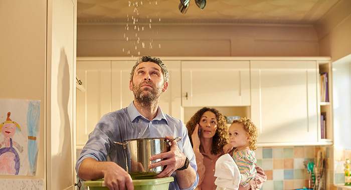 Man using a bowl to catch water dropping from leak in ceiling