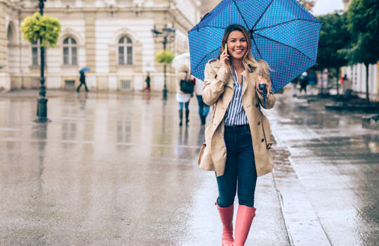 Young woman walking on a street calling someone with a blue umbrella