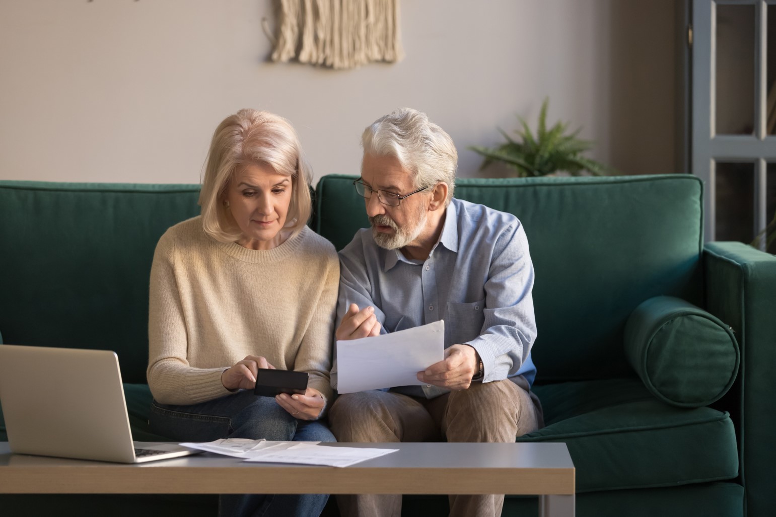 An older man and woman using a calculator while looking at a laptop